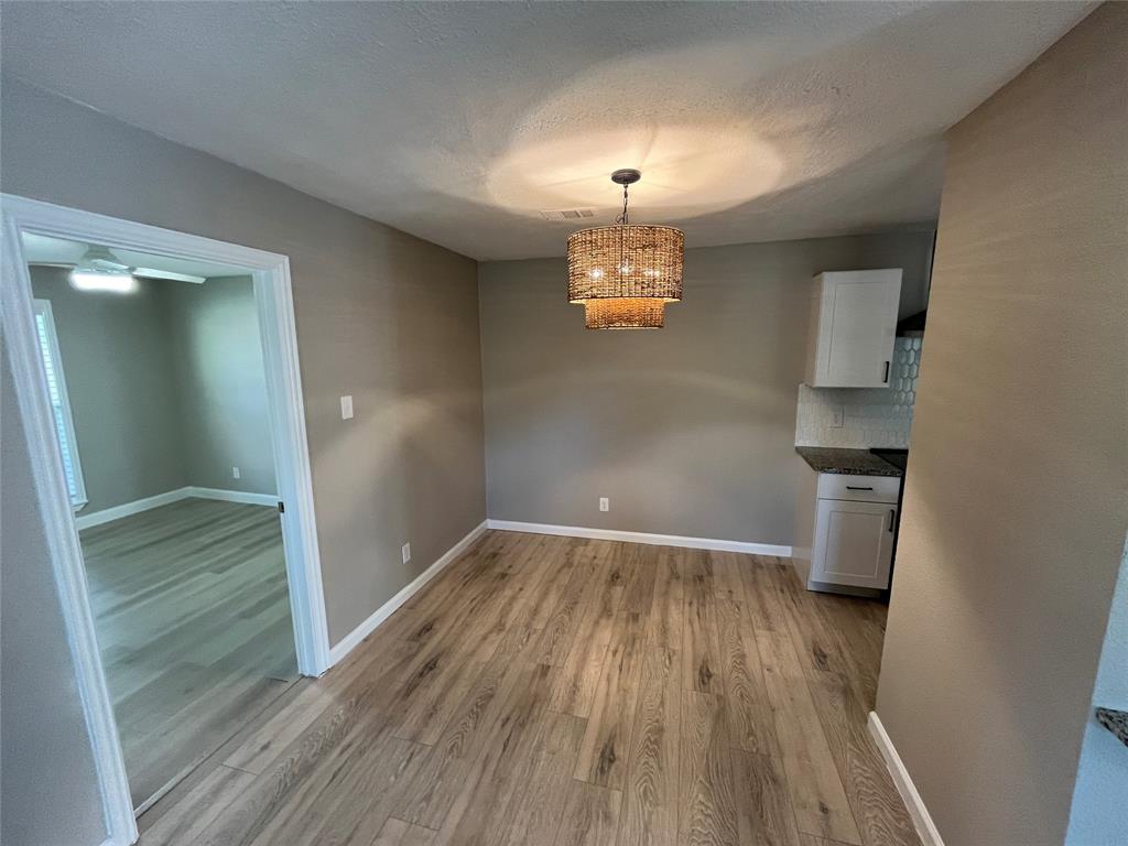 Wood-finish flooring, textured drum pendant lighting, white cabinetry, and a geometric tiled backsplash