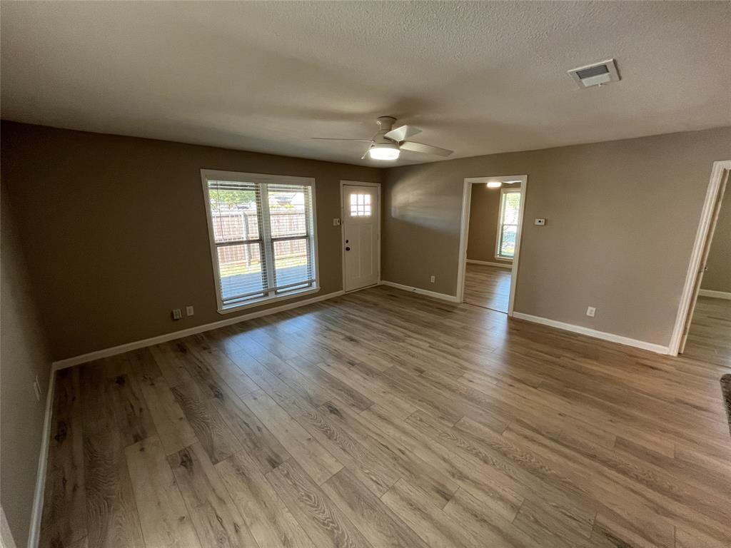 Open-concept interior featuring wood-finish flooring, a multi-pane glass entry door, and a ceiling-mounted light fixture with integrated fan