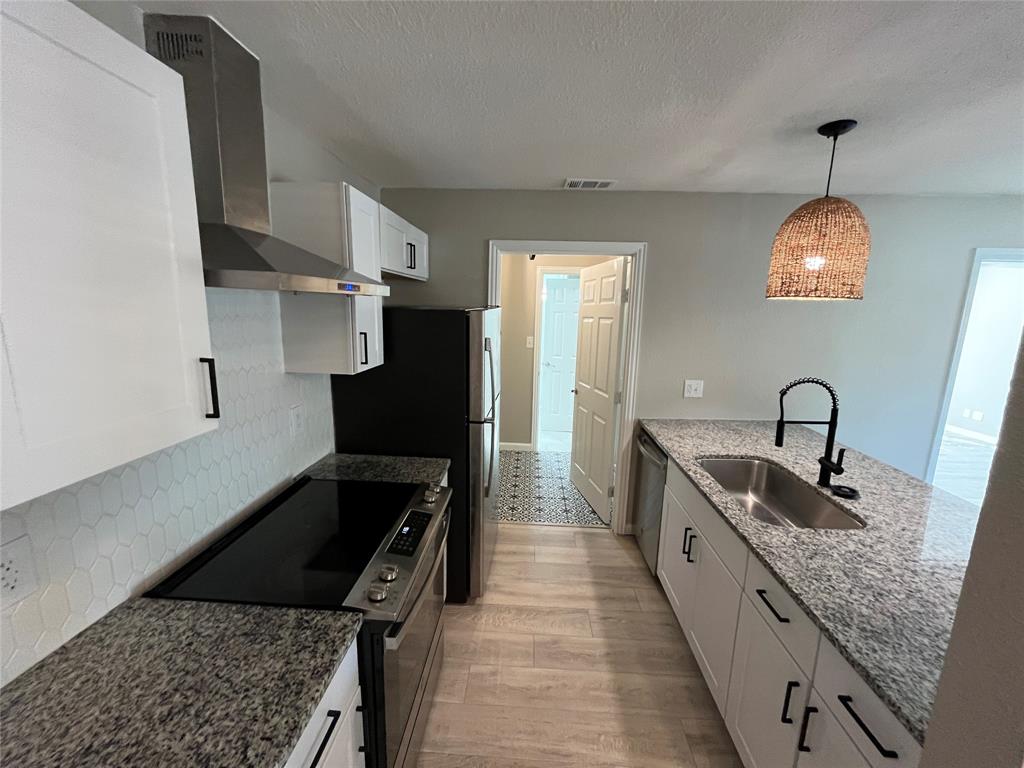 Kitchen featuring shaker-style cabinetry, stone countertops, hexagonal tile backsplash, stainless steel range with overhead ventilation, and a gooseneck faucet