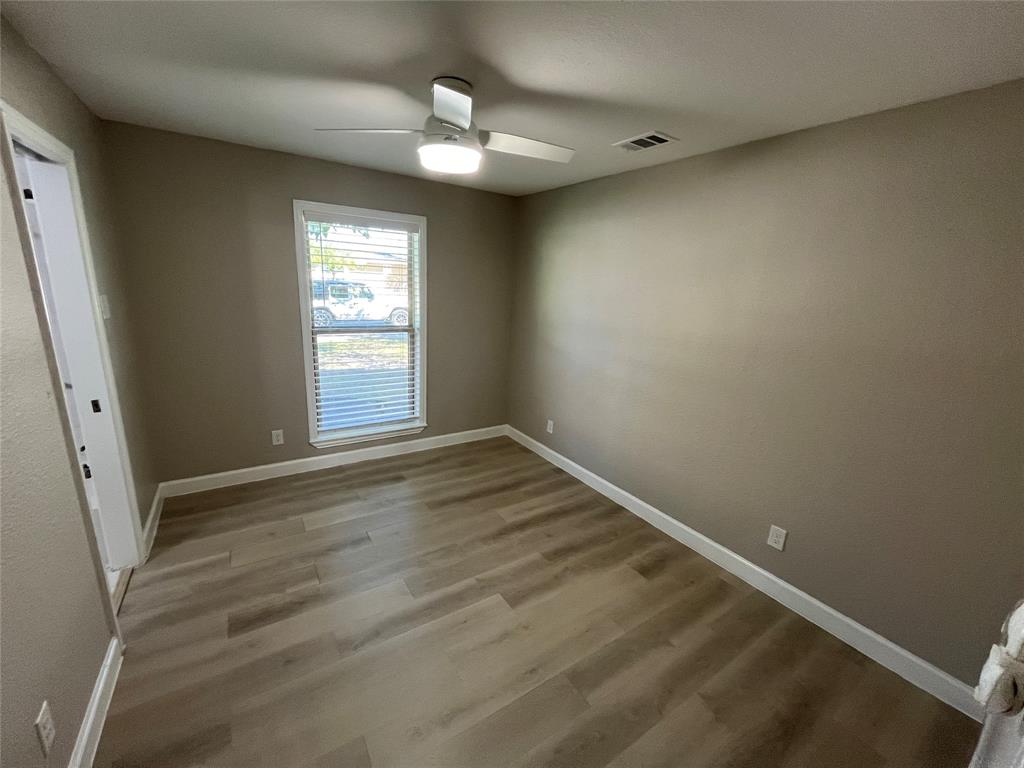 Neutral-toned interior space featuring wood-finish flooring, a ceiling fan with integrated lighting, and a single-pane window with horizontal blinds