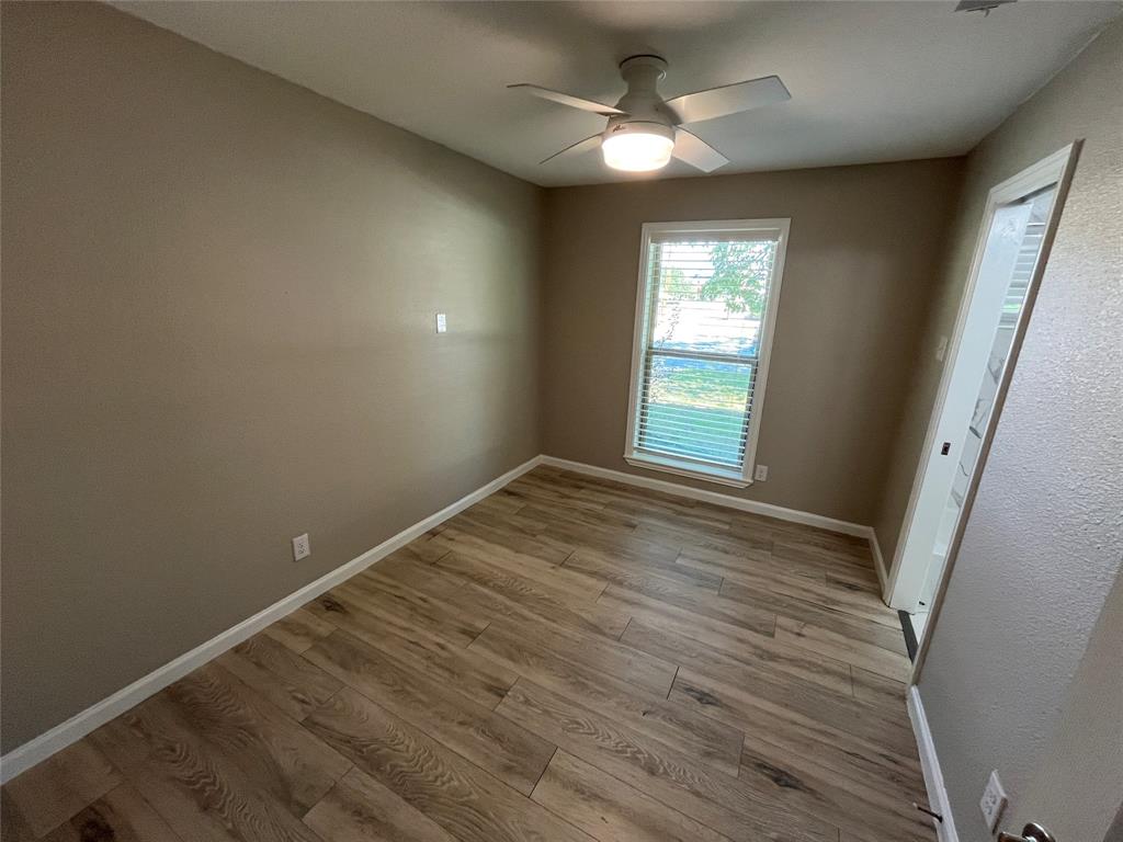 Room featuring wood-finish flooring, a neutral wall palette, an integrated ceiling fan with light fixture, and a window with blinds