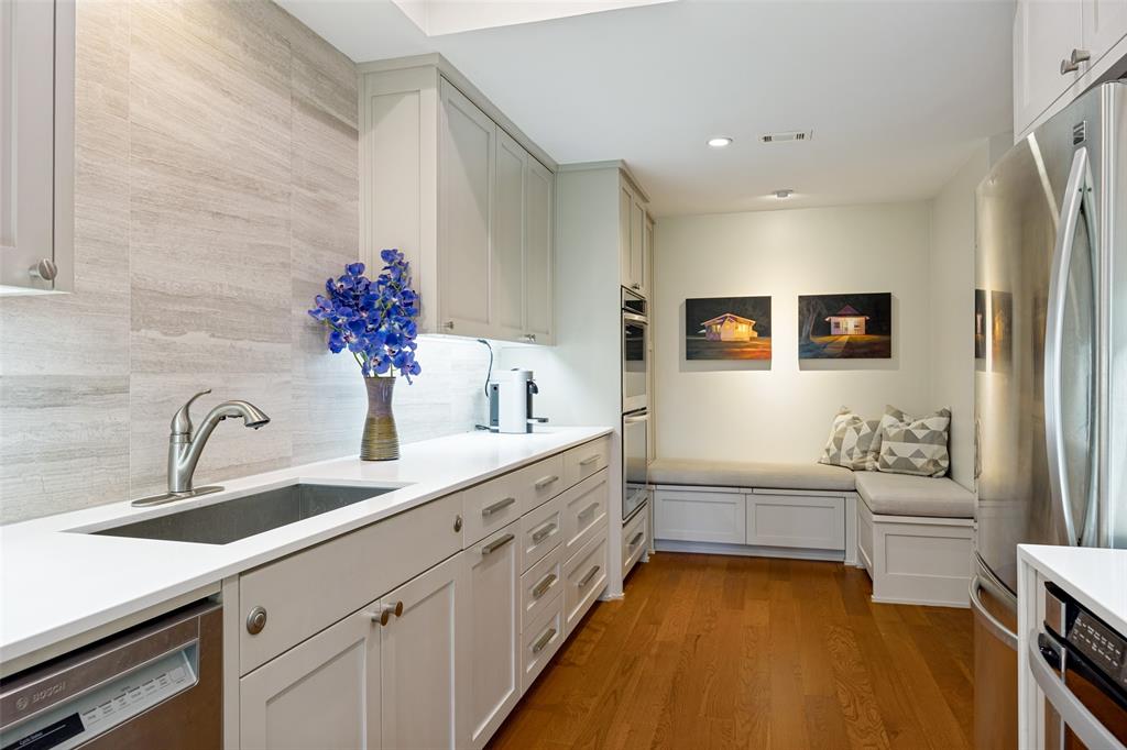 Kitchen featuring light-toned cabinetry, solid surface countertops, a tiled backsplash, built-in wall ovens, and custom bench seating with integrated storage