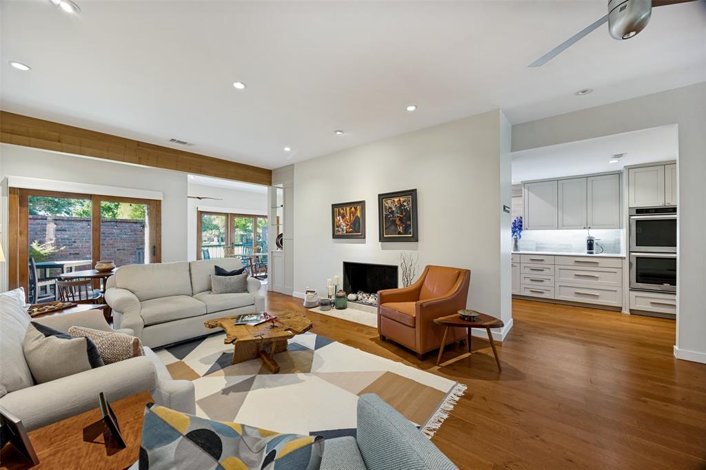 Open-concept living area featuring wood-finish flooring, a recessed fireplace with a stone hearth, exposed timber ceiling beam, sliding glass doors, and recessed lighting