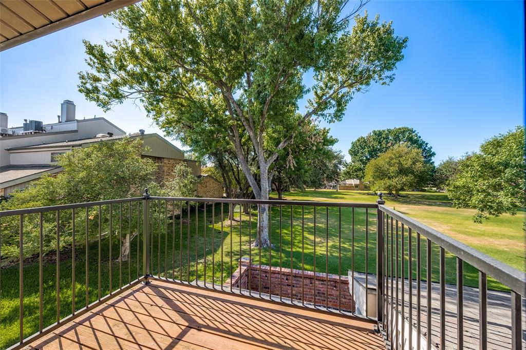 Elevated balcony with metal railing, wood-finish decking, mature trees, and brick hardscaping