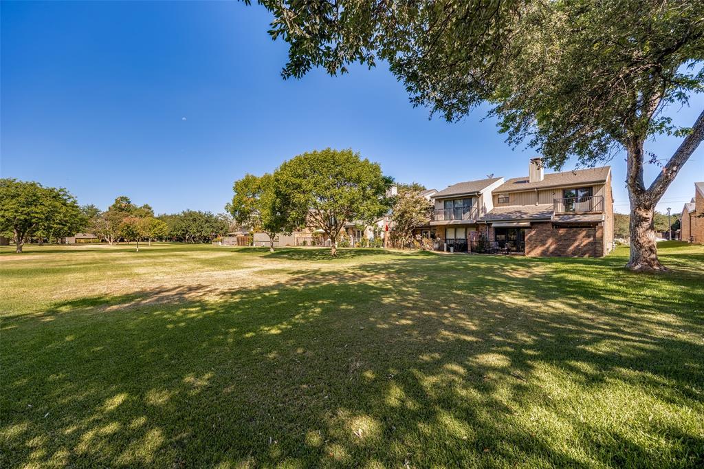 Expansive backyard featuring a manicured lawn, mature trees, and a brick-accented exterior