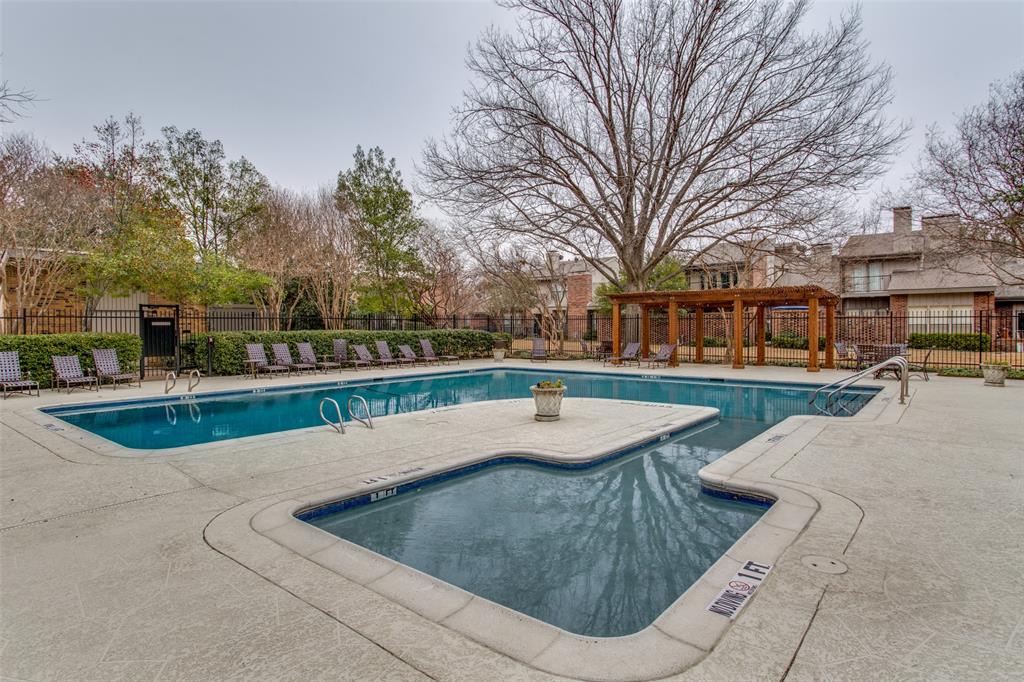 In-ground swimming pool with shallow wading area, surrounding concrete decking, wood-frame pergola, and perimeter metal fencing