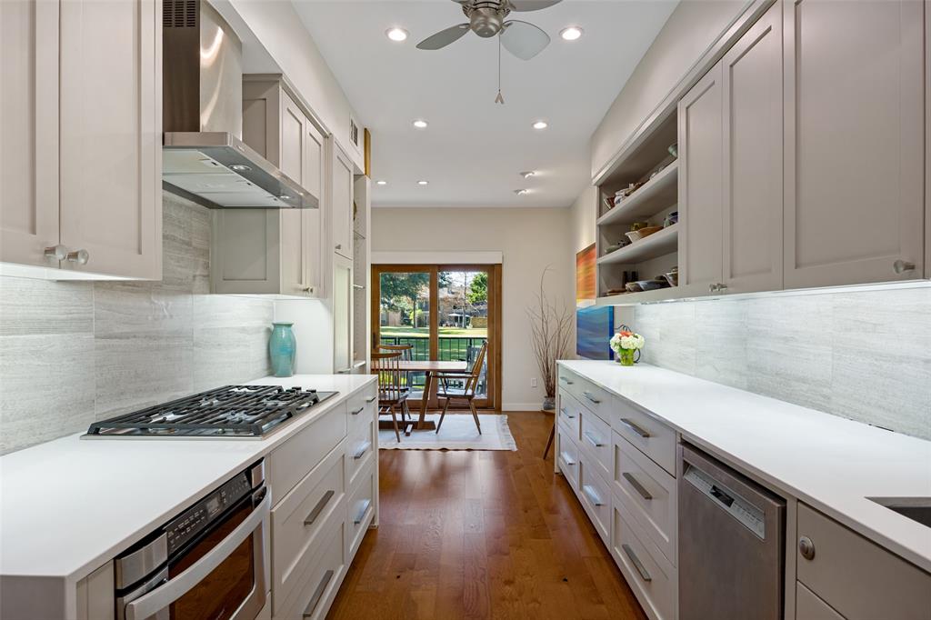 Galley kitchen featuring flat-panel cabinetry, white solid-surface countertops, horizontal-tile backsplash, stainless steel gas cooktop with range hood, and wood-finish flooring