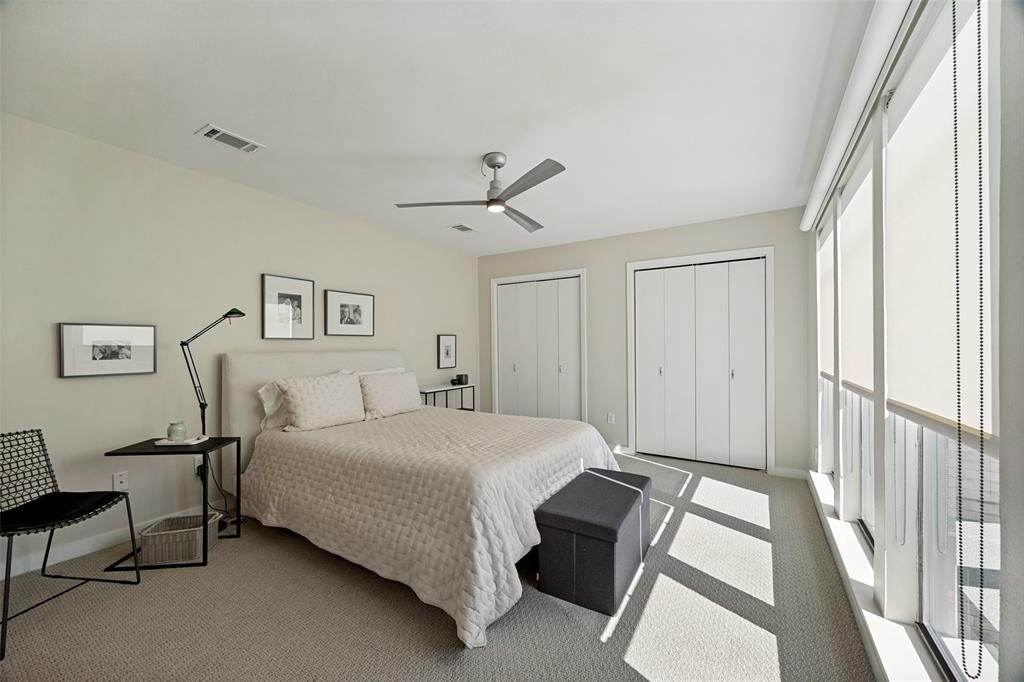 Room featuring neutral wall-to-wall carpeting, floor-to-ceiling windows with roller shades, a ceiling fan with integrated lighting, and dual closets with bifold doors
