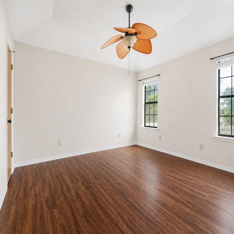 Vaulted ceiling room featuring wood-finish flooring, a multi-blade ceiling fan with integrated light, and grid-pattern windows with dark frames