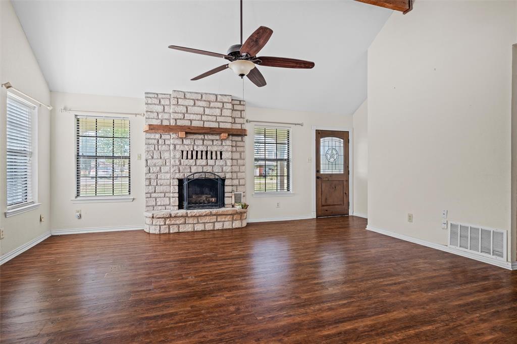 Living area featuring a floor-to-ceiling masonry fireplace with a wooden mantel, vaulted ceilings, wood-finish flooring, and a stained wood entry door with decorative glass inlay