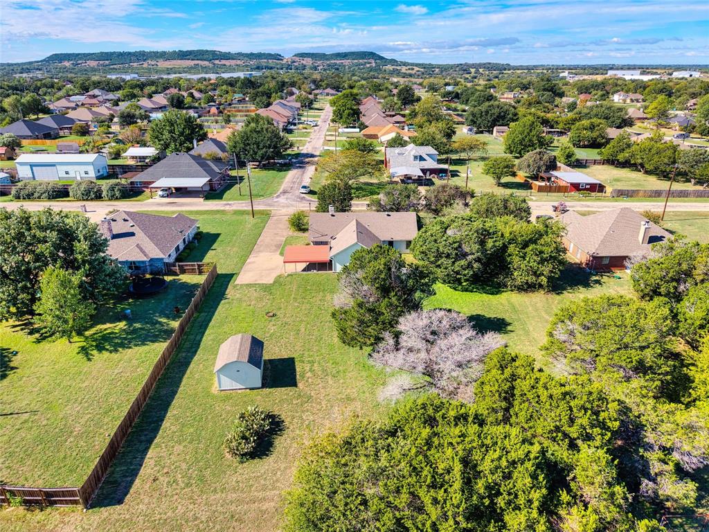 Expansive residential lot featuring a detached storage structure, concrete driveway, attached carport, and mature trees