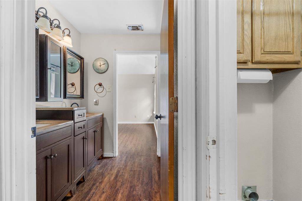 Bathroom vanity with dark-finish cabinetry, solid-surface countertop, and integrated dual sinks, featuring multi-bulb overhead lighting and wood-finish flooring