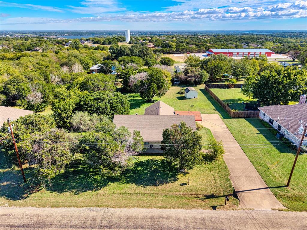 Aerial perspective of a multi-structure property featuring a long concrete driveway, shingle-roofed residence, detached storage shed, and expansive grounds with mature trees
