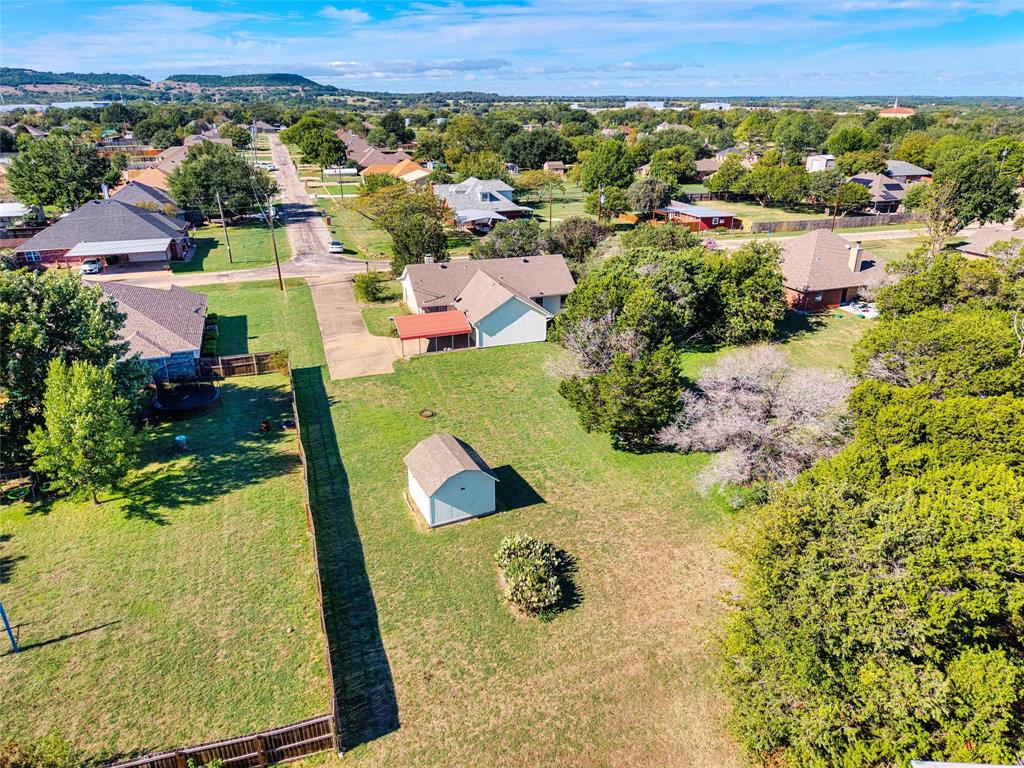 Expansive parcel featuring mature trees, a detached storage structure, wooden perimeter fencing, and concrete driveway access