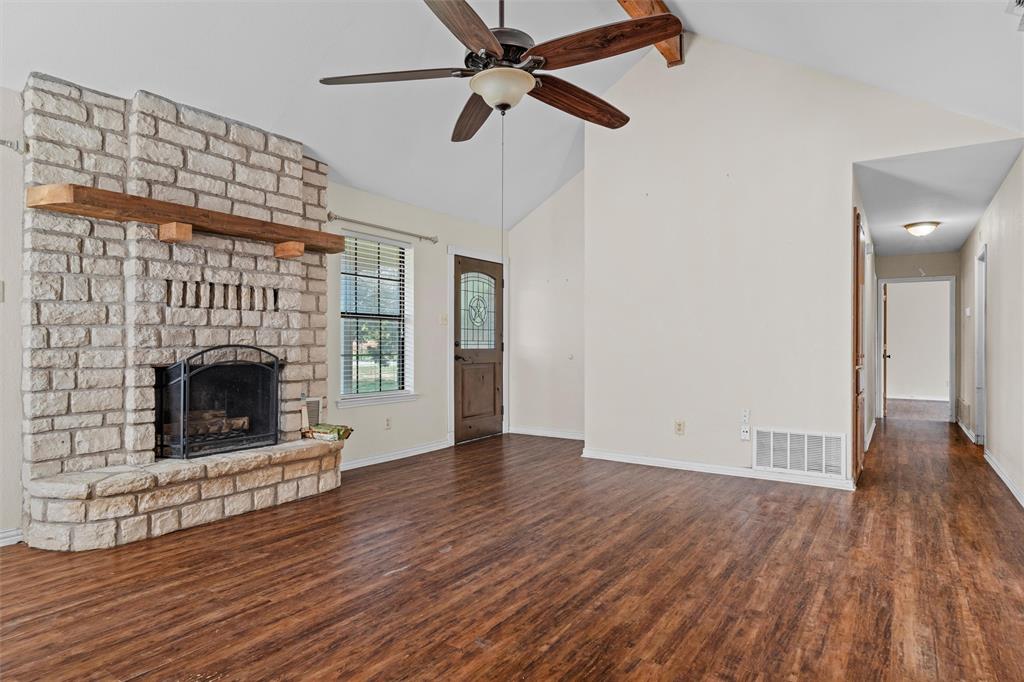 Vaulted ceilings featuring a prominent wooden beam, stone fireplace with a thick timber mantel, and wood-finish flooring