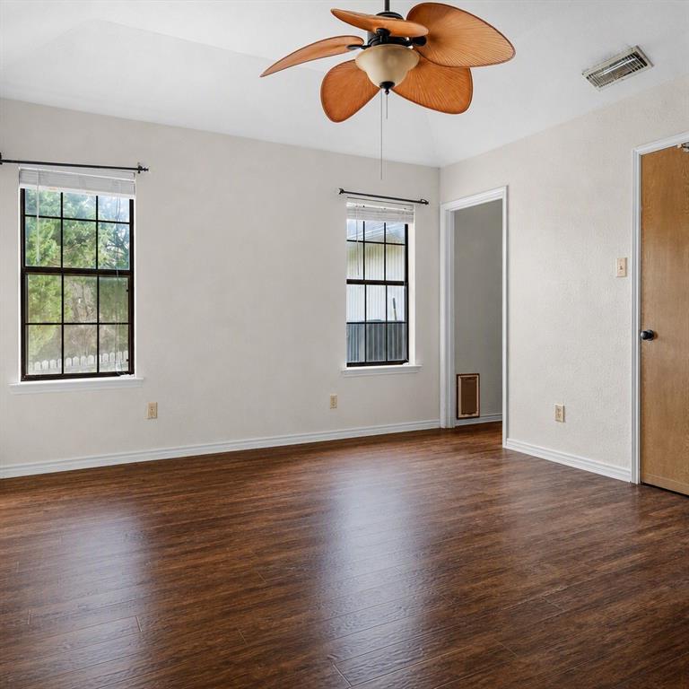 Interior space featuring dark wood-finish flooring, vaulted ceilings, dual-pane windows with grid mullions, and a decorative ceiling fan