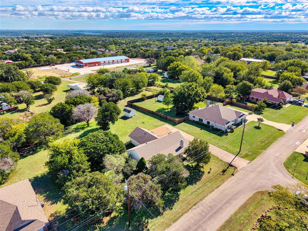 Aerial perspective featuring expansive acreage, mature tree canopy, stone-accented residence, and cleared lawn space