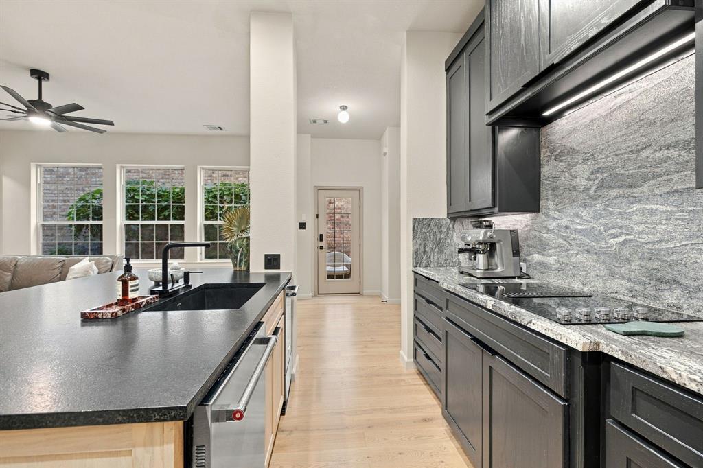 Kitchen featuring dark cabinetry, expansive stone countertops, stone slab backsplash with integrated lighting, undermount sink with matte black faucet, and light-tone wood-finish flooring