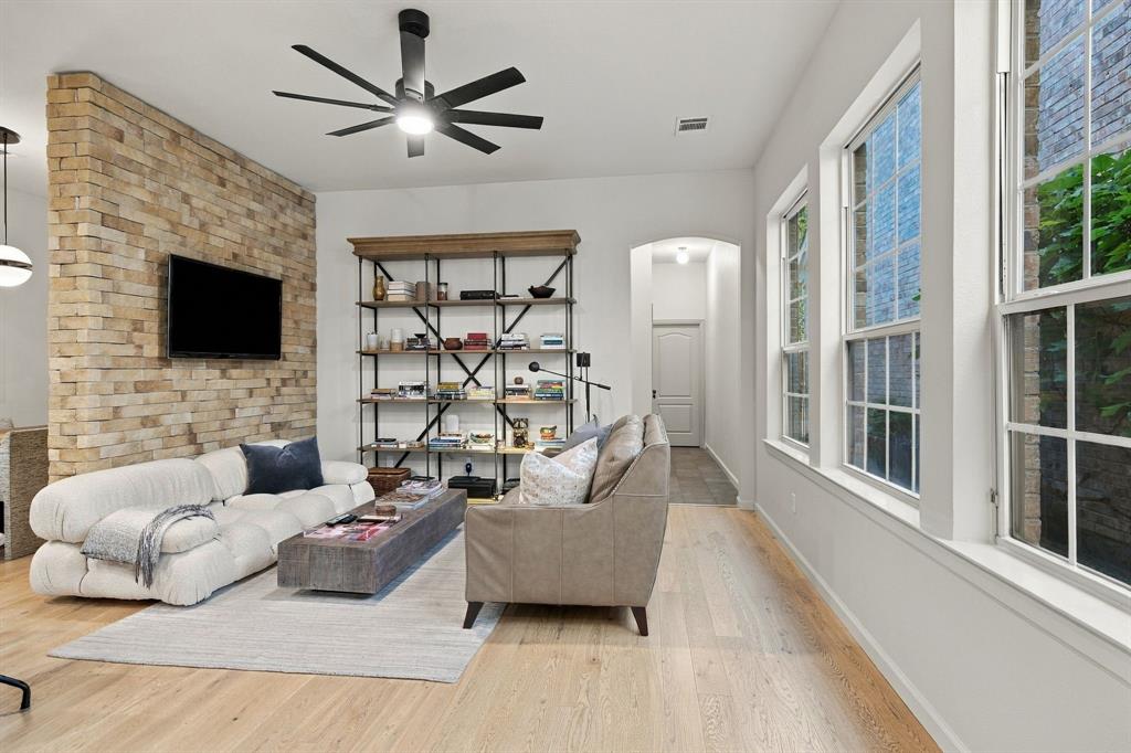 Textured stone accent wall, light-toned wood-finish flooring, multi-pane windows, and a matte black multi-blade ceiling fan