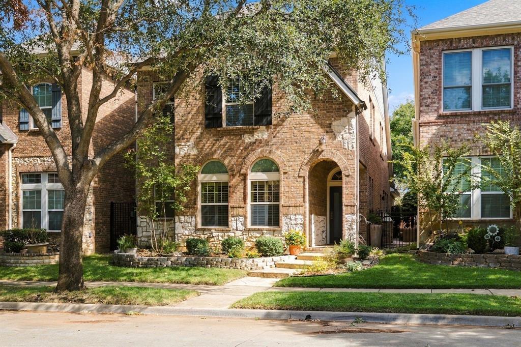 Two-story brick exterior featuring stone masonry accents, arched window detailing, shuttered windows, and a covered entryway