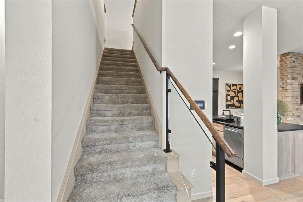 Staircase featuring wall-to-wall carpeting, wood-finish handrail, glass paneling, and black metal supports