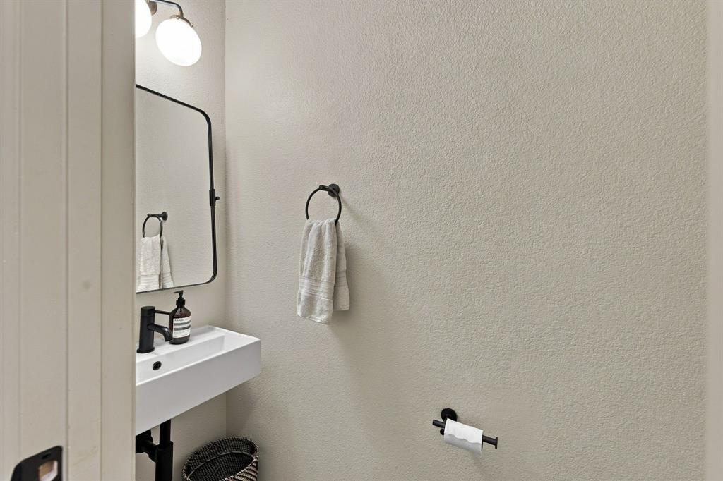 Wall-mounted rectangular sink with a matte black faucet, rounded rectangular mirror, and matching matte black hardware