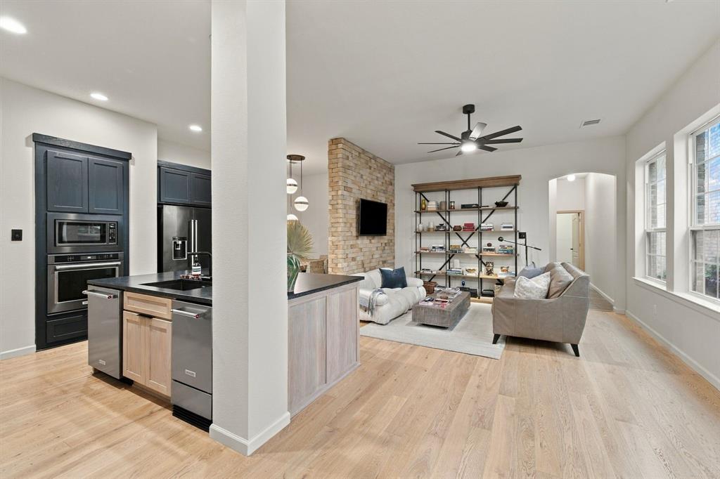 Kitchen featuring wood-finish flooring, dark cabinetry, stainless steel built-in appliances, and a central island with a stone surface