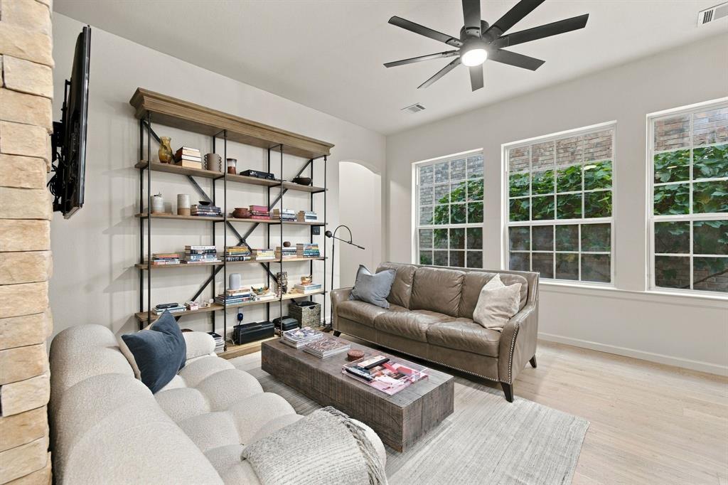 Built-in metal and wood shelving unit, stone-accented wall, wood-finish flooring, and multi-pane windows with a modern ceiling fan