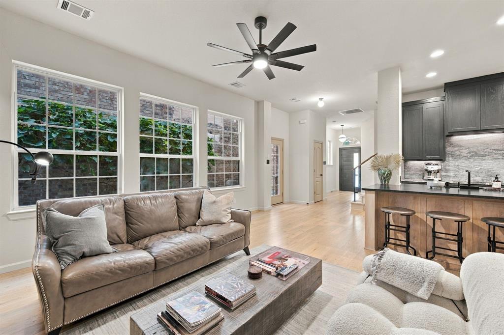 Open concept interior featuring wood-finish flooring, multi-pane windows, a dark-finish kitchen island with stone-surface countertop, and a contemporary ceiling fan