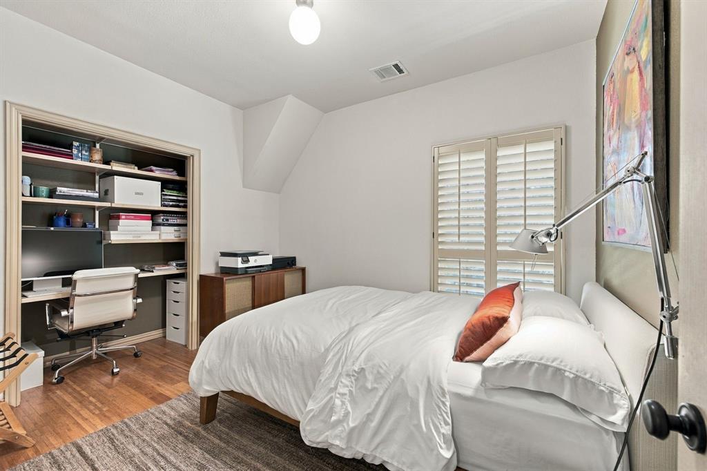 Bedroom featuring wood-finish flooring, built-in shelving, plantation shutters, and a wall-mounted adjustable lamp