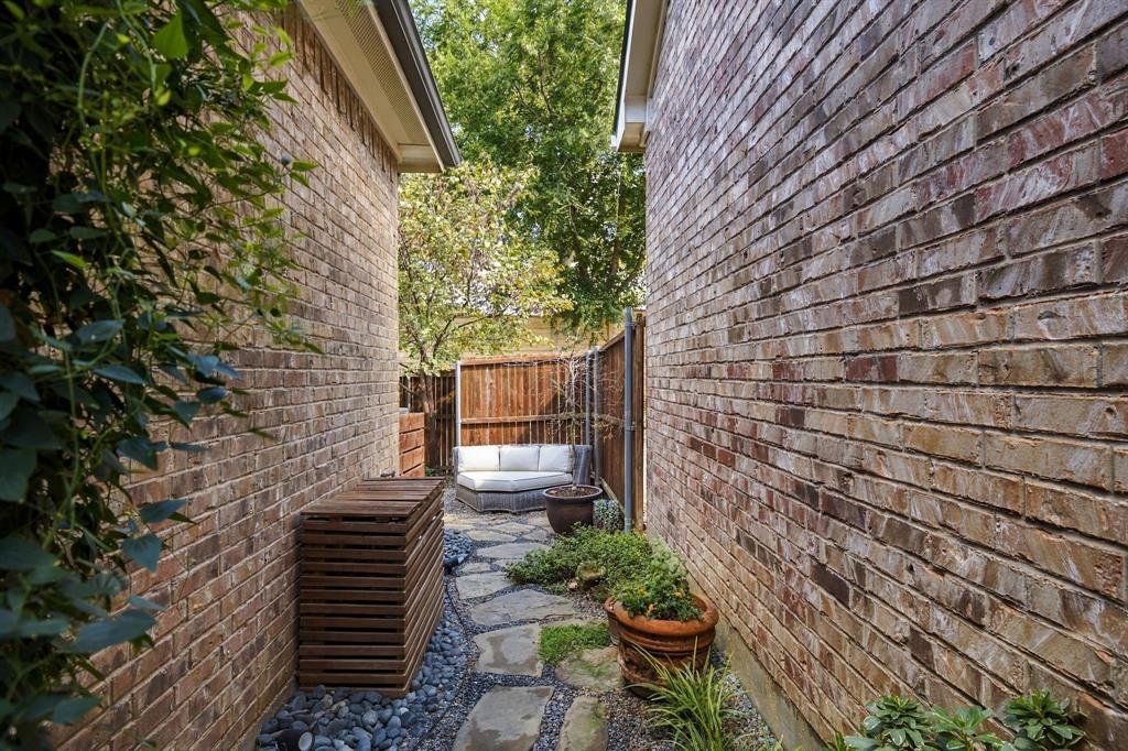 Side yard featuring a stone pathway, natural river rock borders, and full-height brick exterior walls enclosed by wood privacy fencing