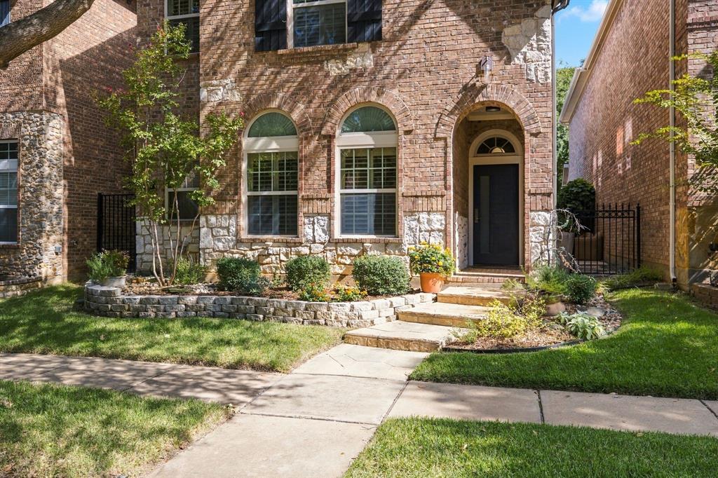 Brick and stone veneer facade featuring arched windows with muntins, a covered arched entryway, and stone-retaining garden beds
