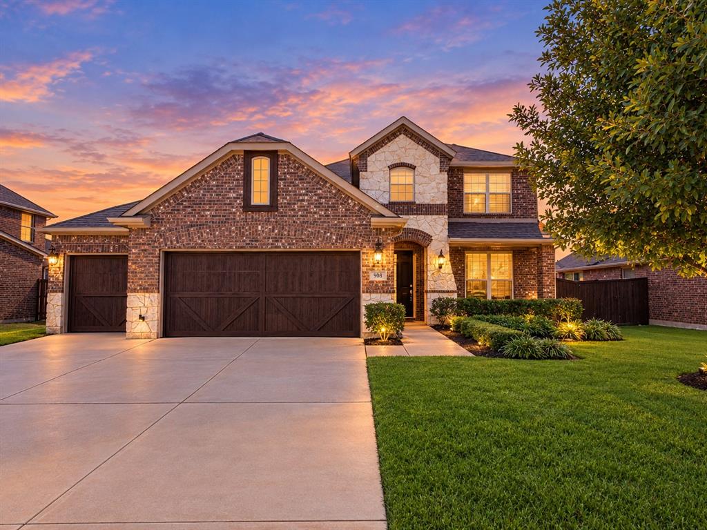 Multi-level brick and stone facade featuring a three-car garage with dark wood-finish carriage doors, a concrete driveway, and landscaped front lawn
