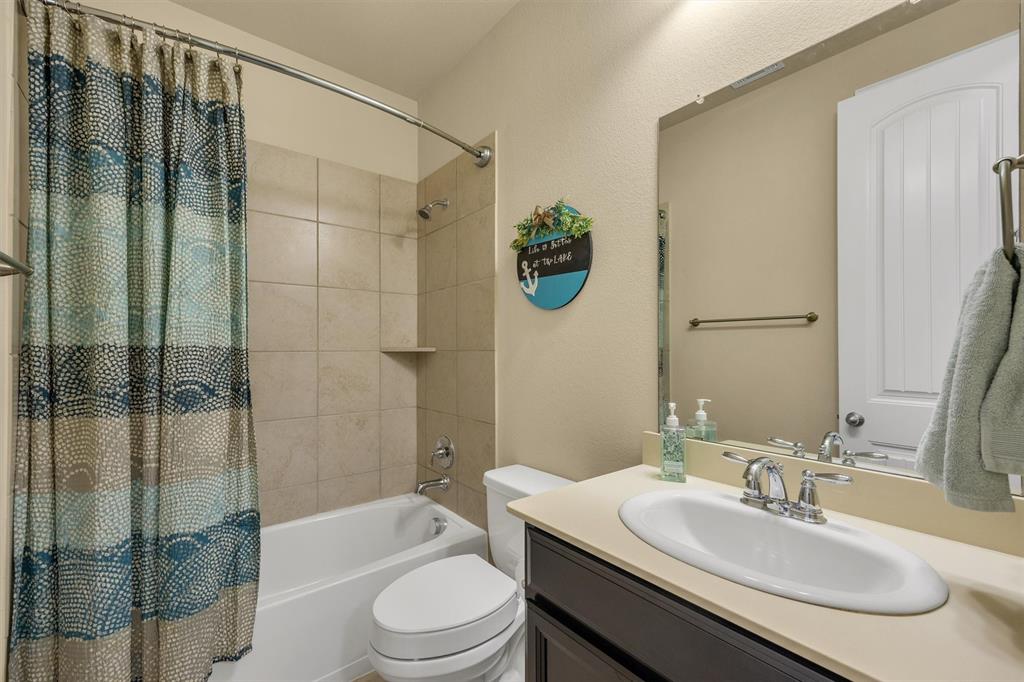 Bathroom featuring a dark-finish vanity with a light-toned countertop, a drop-in porcelain sink, a full-width vanity mirror, and a tub-shower combination with tile surround