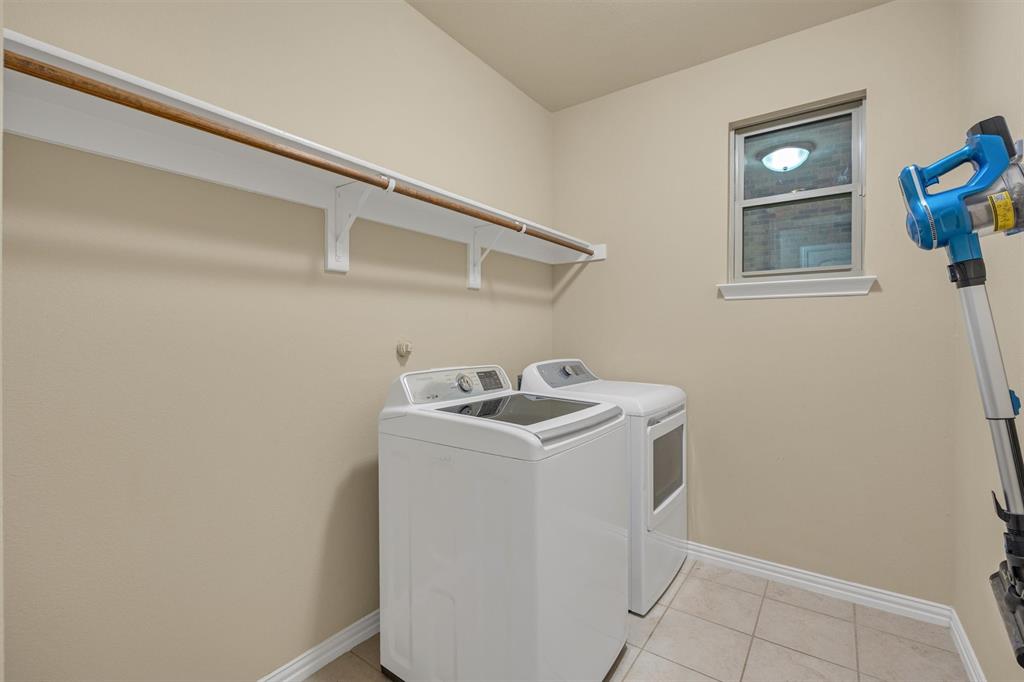 Utility area featuring neutral tile flooring, built-in wall-mounted shelving with a clothes rod, and a single-pane window