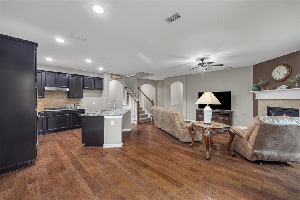 Open-concept living space featuring wood-finish flooring, dark cabinetry, stone-finish countertops, recessed lighting, and a fireplace with a stone-finish surround