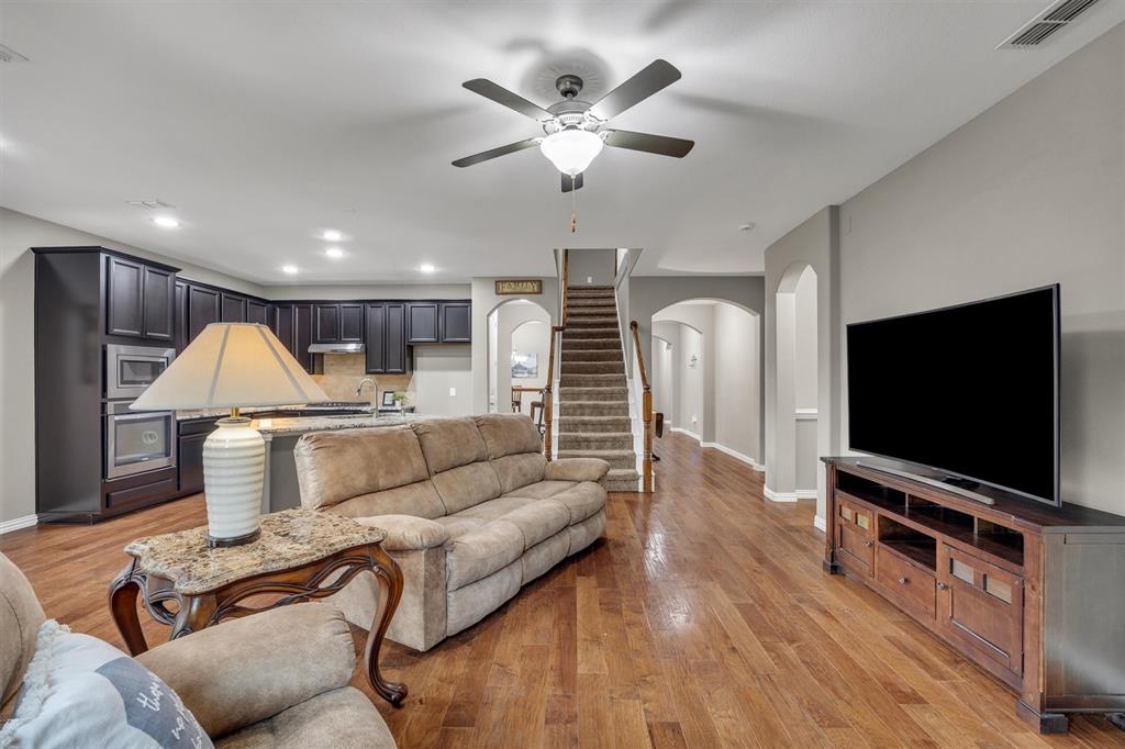 Open-concept interior featuring dark-toned built-in cabinetry, recessed lighting, wood-finish flooring, a kitchen island with stone-finish countertops, and an arched entryway