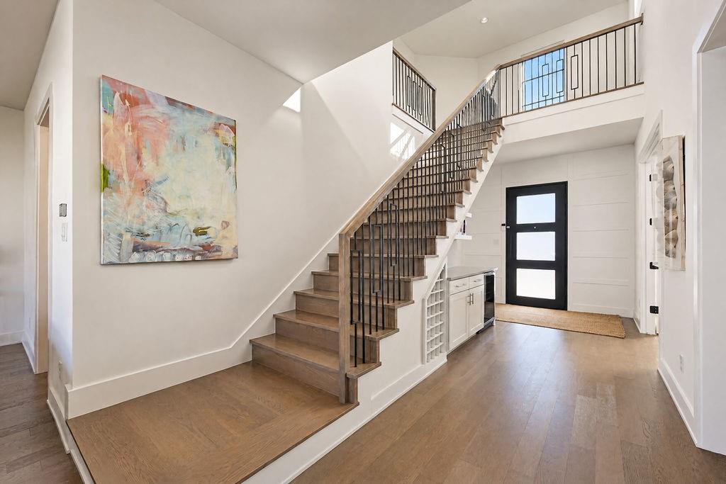Hardwood floors sweep past the open staircase and custom dry bar, setting an inviting tone the moment you walk through the door