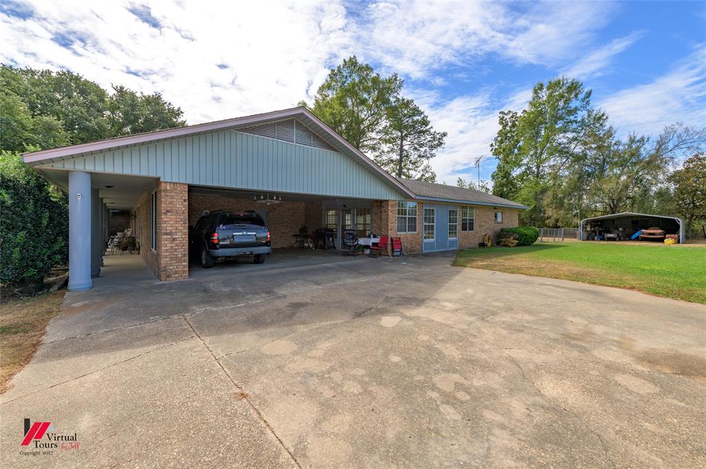 Exterior featuring a brick facade, expansive concrete driveway, covered parking area, and detached metal structure