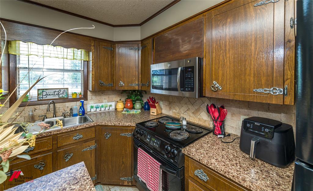 Kitchen featuring wood cabinetry with decorative metal hardware, laminate countertops, a stone-tiled backsplash in a herringbone pattern, and stainless steel microwave