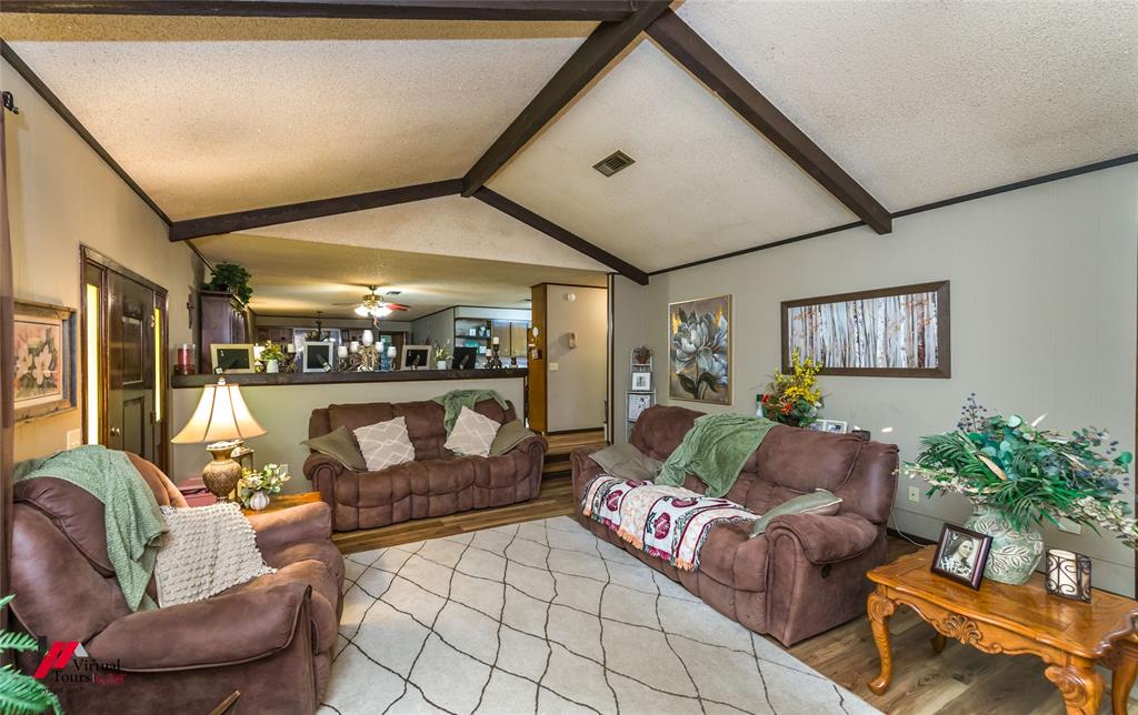 Vaulted ceiling with exposed decorative wood beams, textured ceiling finish, and wood-finish flooring