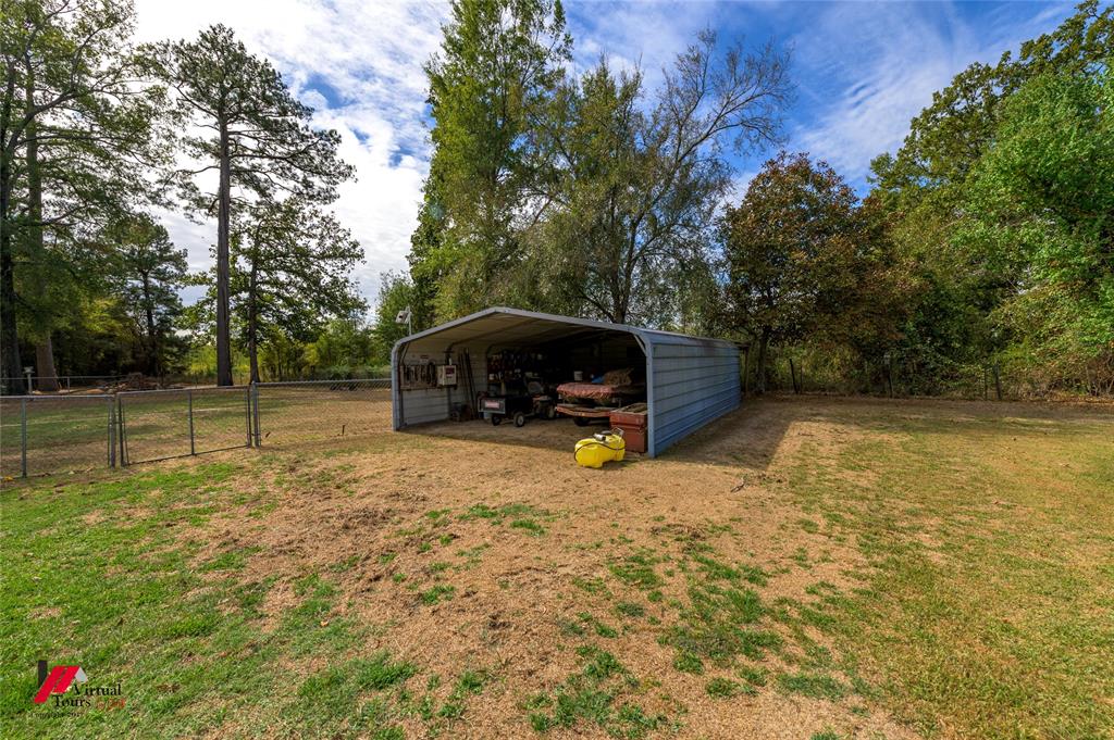 Metal-frame carport structure, chain-link perimeter fencing, and mature trees situated on an open lot