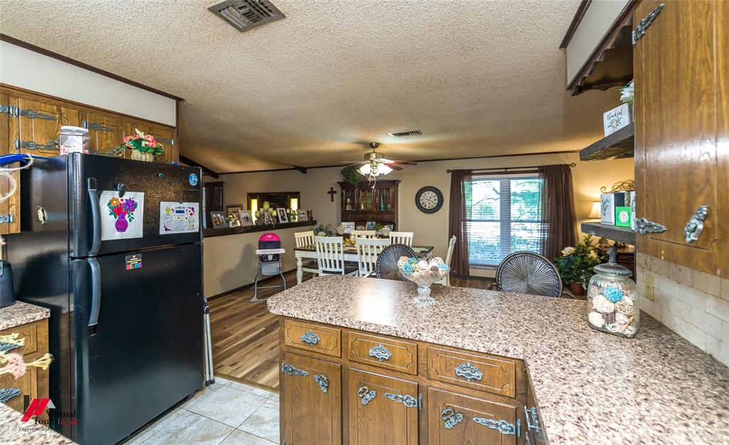Kitchen featuring wood cabinetry with decorative hardware, speckled laminate countertops, tile flooring, and wood-finish flooring in the additional area