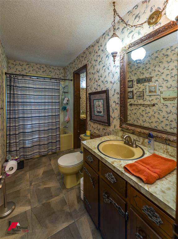 Bathroom featuring stone-finish countertop, dark wood-finish cabinetry, patterned wall covering, oversized framed mirror, and tile flooring