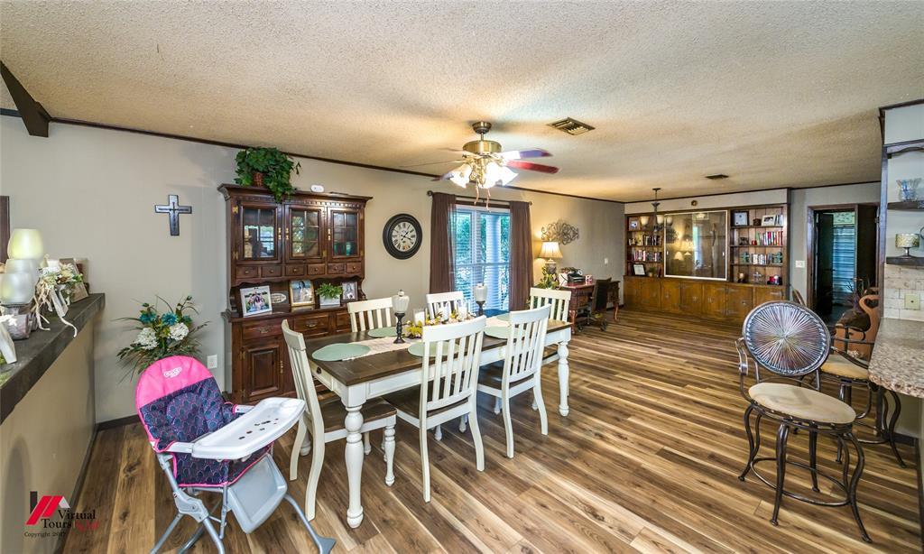 Open-concept interior featuring wood-finish flooring, built-in wooden cabinetry with glass-front shelving, and a ceiling-mounted light fixture with a fan