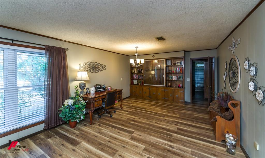 Living area featuring wood-finish flooring, extensive built-in wood cabinetry with shelving, multi-arm chandelier, and a large window