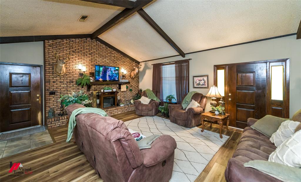 Vaulted ceiling with exposed decorative beams, full-height brick masonry fireplace, and wood-finish flooring
