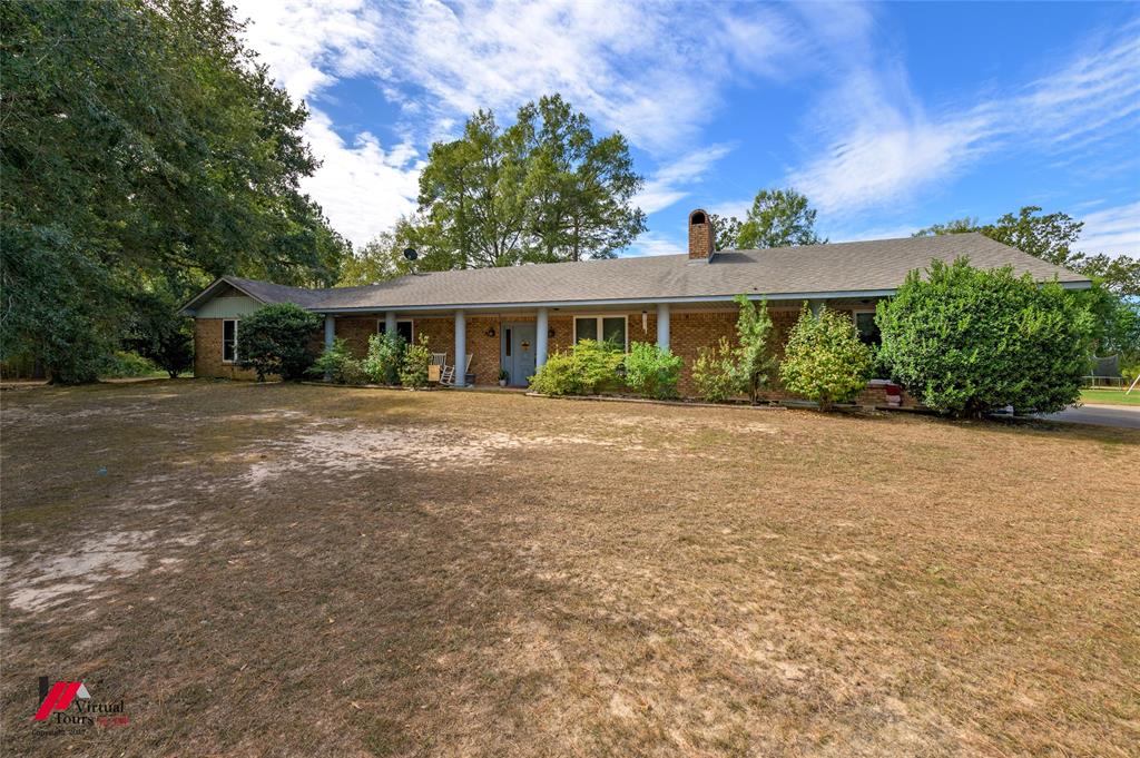 Single-story ranch exterior featuring a brick facade, covered front porch with support columns, asphalt shingle roof, and a prominent brick chimney