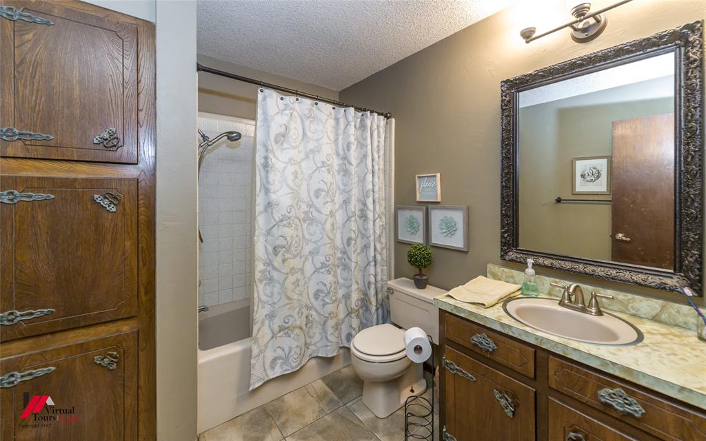 Bathroom featuring a stone-look countertop, wood cabinetry with metal hardware, built-in floor-to-ceiling storage, tiled tub surround, and a framed mirror with overhead vanity lighting