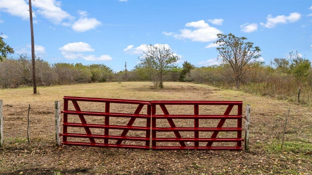 Expansive acreage featuring a metal tubular gate, wire fencing, and mature trees